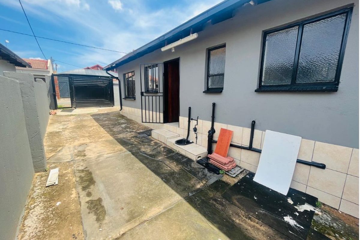 Rear exterior view of the property featuring a concrete driveway, security gate, and external plumbing along the side wall.