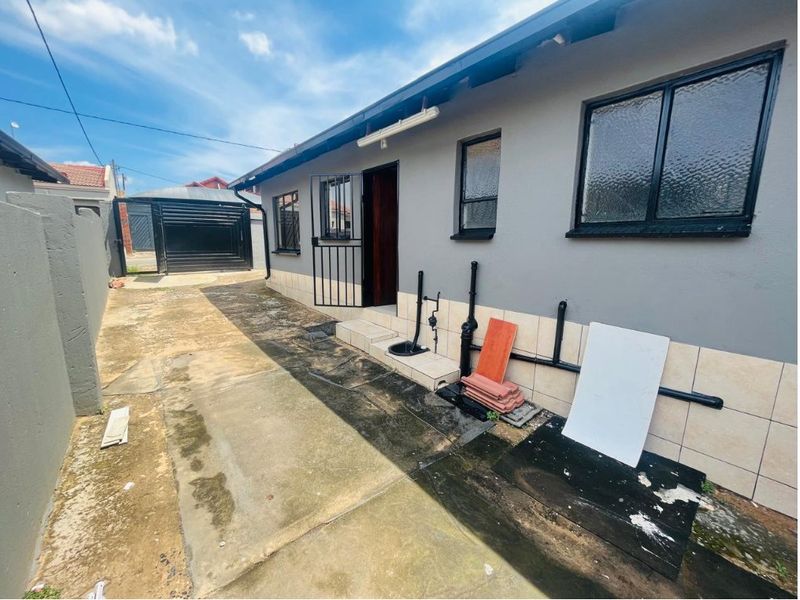 Rear exterior view of the property featuring a concrete driveway, security gate, and external plumbing along the side wall.