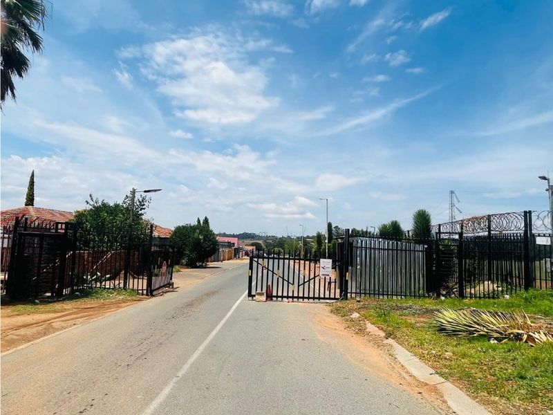 A view of a residential street entrance featuring a security gate and perimeter fencing with razor wire.