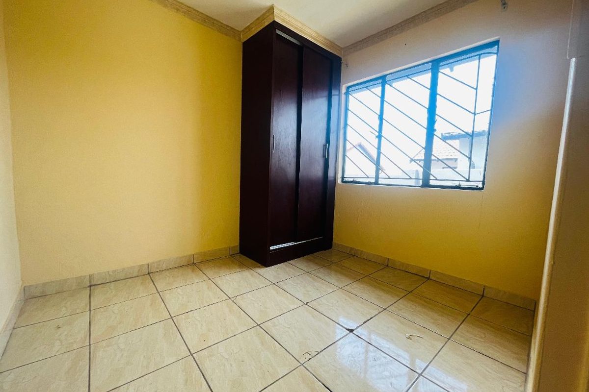 An empty bedroom featuring tiled flooring, a built-in wardrobe, and security bars on the window.