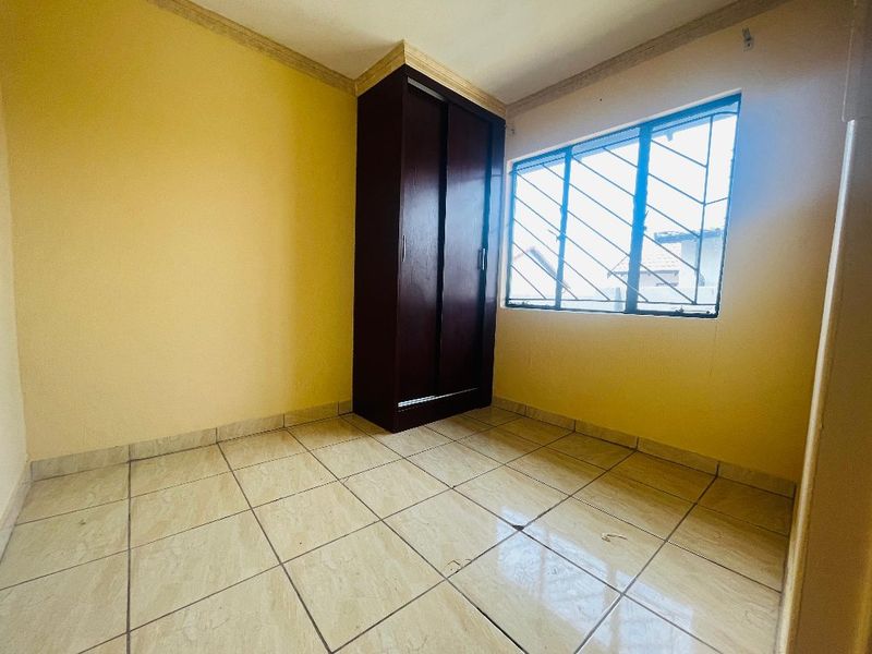 An empty bedroom featuring tiled flooring, a built-in wardrobe, and security bars on the window.