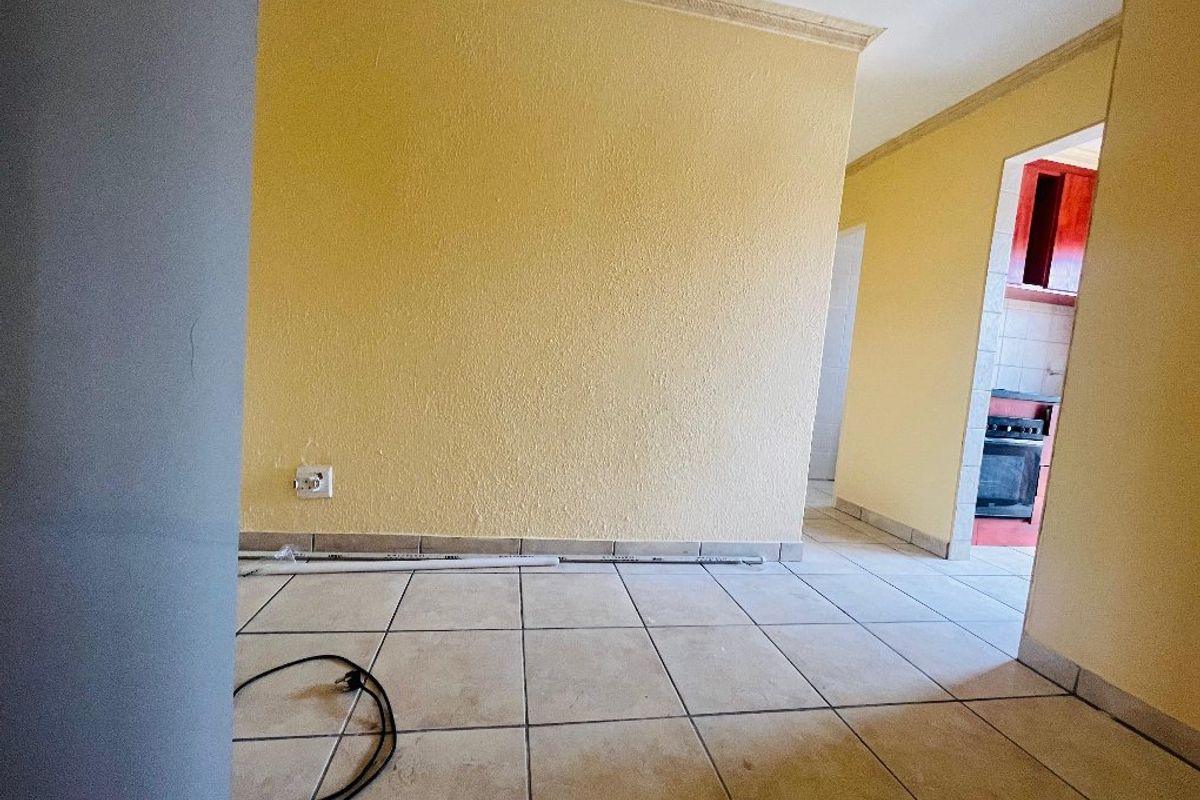 An empty living area featuring ceramic floor tiles and coved ceiling cornices, with a view through to the kitchen area.