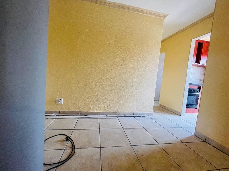 An empty living area featuring ceramic floor tiles and coved ceiling cornices, with a view through to the kitchen area.