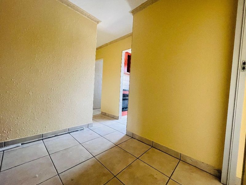 A vacant hallway featuring tiled flooring and yellow walls, providing access to adjacent rooms including a kitchen area.