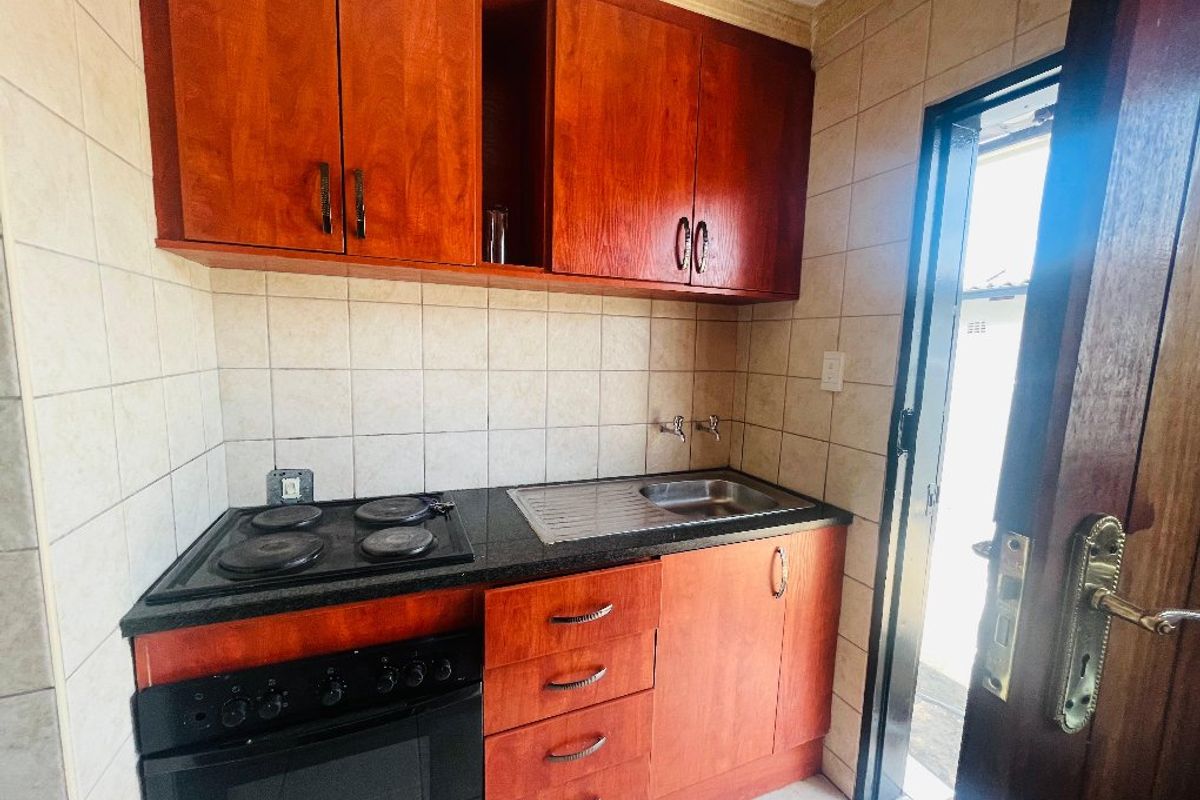 Compact kitchen featuring wooden cabinetry, a built-in electric oven and hob, stainless steel sink, and tiled finishes throughout.