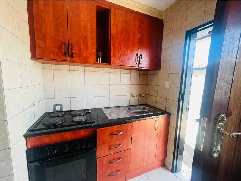 Compact kitchen featuring wooden cabinetry, a built-in electric oven and hob, stainless steel sink, and tiled finishes throughout.