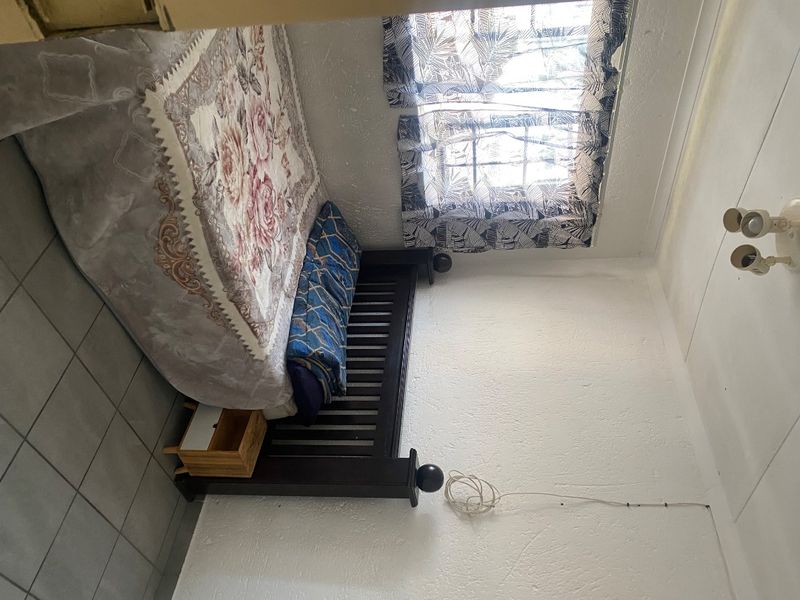 A bedroom featuring tiled flooring and textured walls, currently requiring maintenance due to visible exposed wiring and dated finishes.