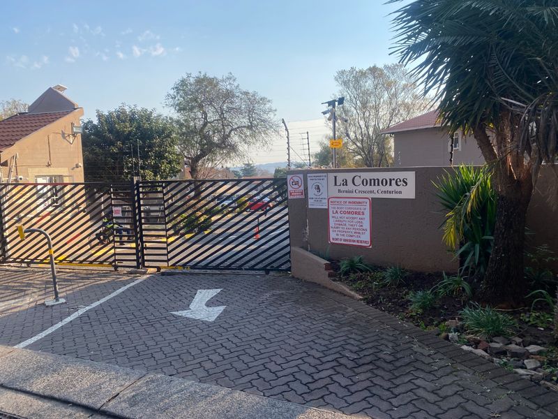 The entrance to La Comores complex in Bernini Crescent, featuring a secure gated access point, paved driveway, and perimeter wall with electric fencing.