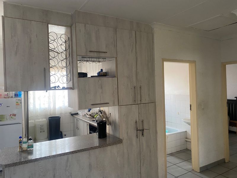 Kitchen area featuring light wood-look cabinetry, stone-effect countertops, and a breakfast bar, with an adjacent doorway leading to a tiled bathroom.