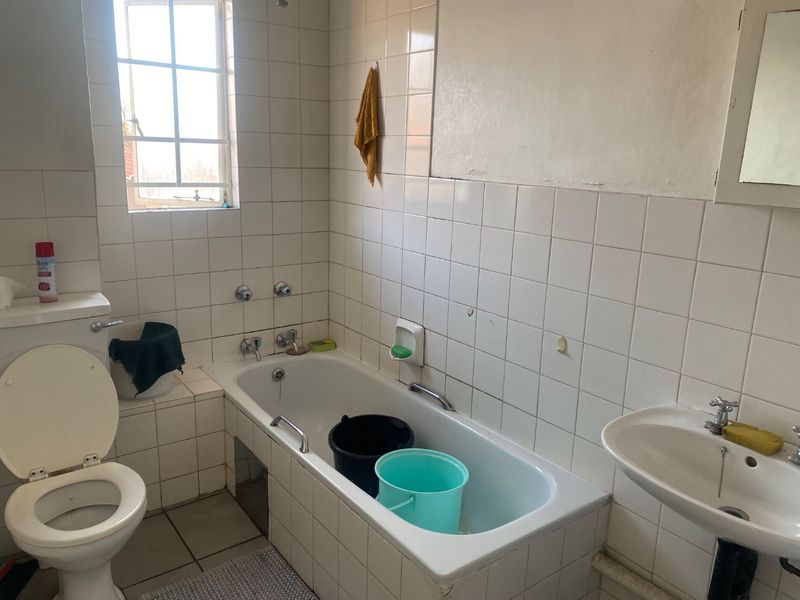 A dated bathroom featuring a standard bathtub, pedestal basin, and toilet with white wall tiling throughout.