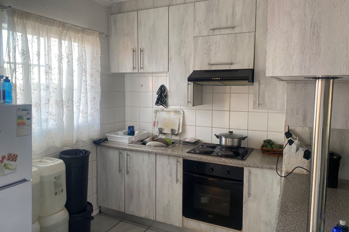 Compact kitchen featuring light wood-grain cabinetry, laminate countertops, tiled backsplash, and integrated appliances including an oven, hob, and extractor fan.