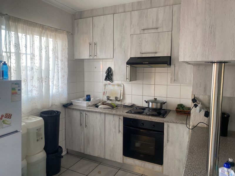 Compact kitchen featuring light wood-grain cabinetry, laminate countertops, tiled backsplash, and integrated appliances including an oven, hob, and extractor fan.