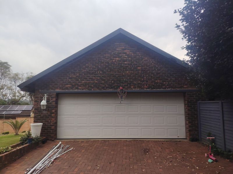 A detached brick garage featuring a sectional door and a paved driveway area.
