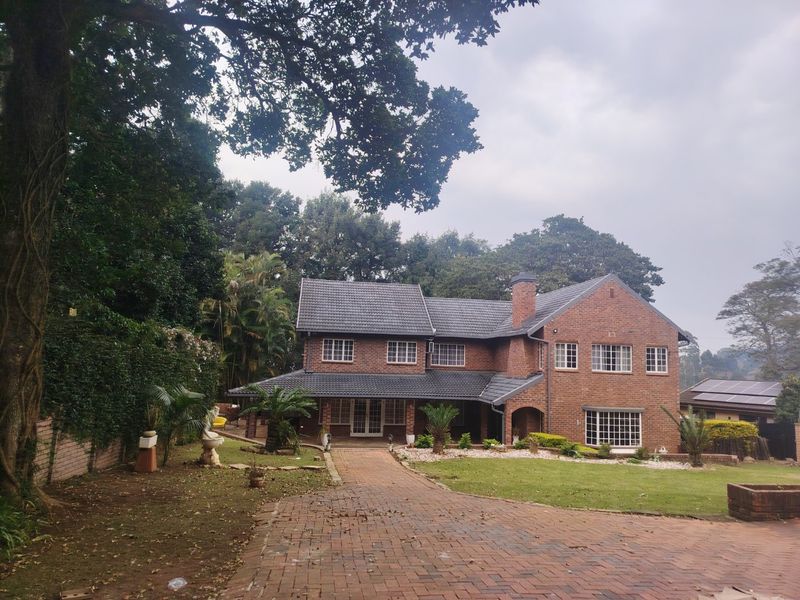 A charming double-story brick residence featuring a tiled roof, covered porch, and a spacious paved driveway set within a mature, landscaped garden.