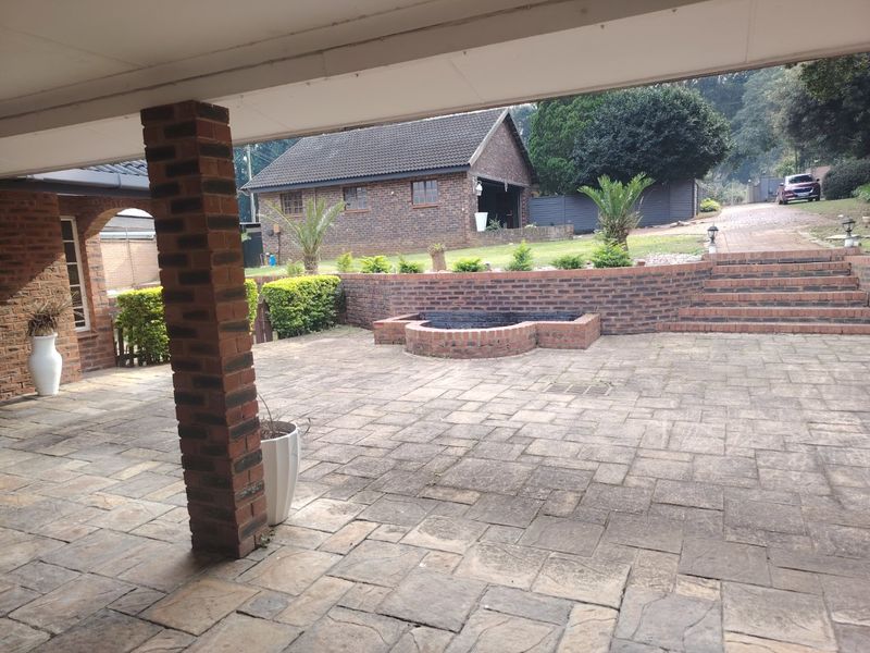 A spacious covered patio featuring brick paving, a built-in brick fire pit, and tiered brick retaining walls leading to a landscaped garden area.