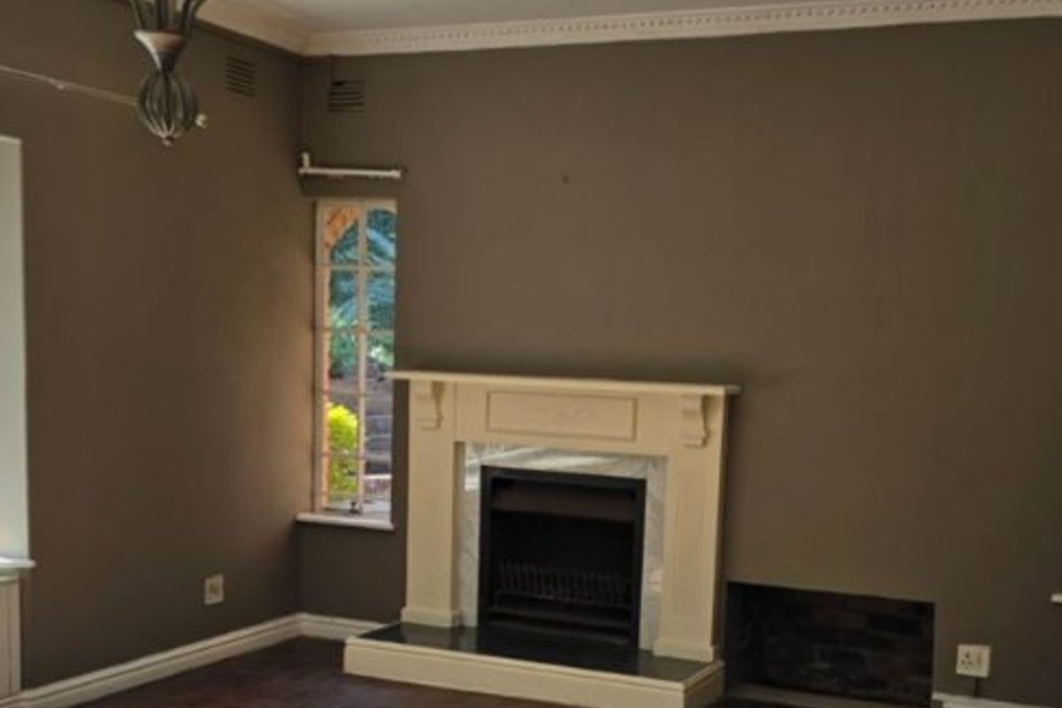 Spacious living room featuring dark parquet flooring, a classic fireplace with a mantelpiece, decorative ceiling cornicing, and a traditional wrought iron chandelier.
