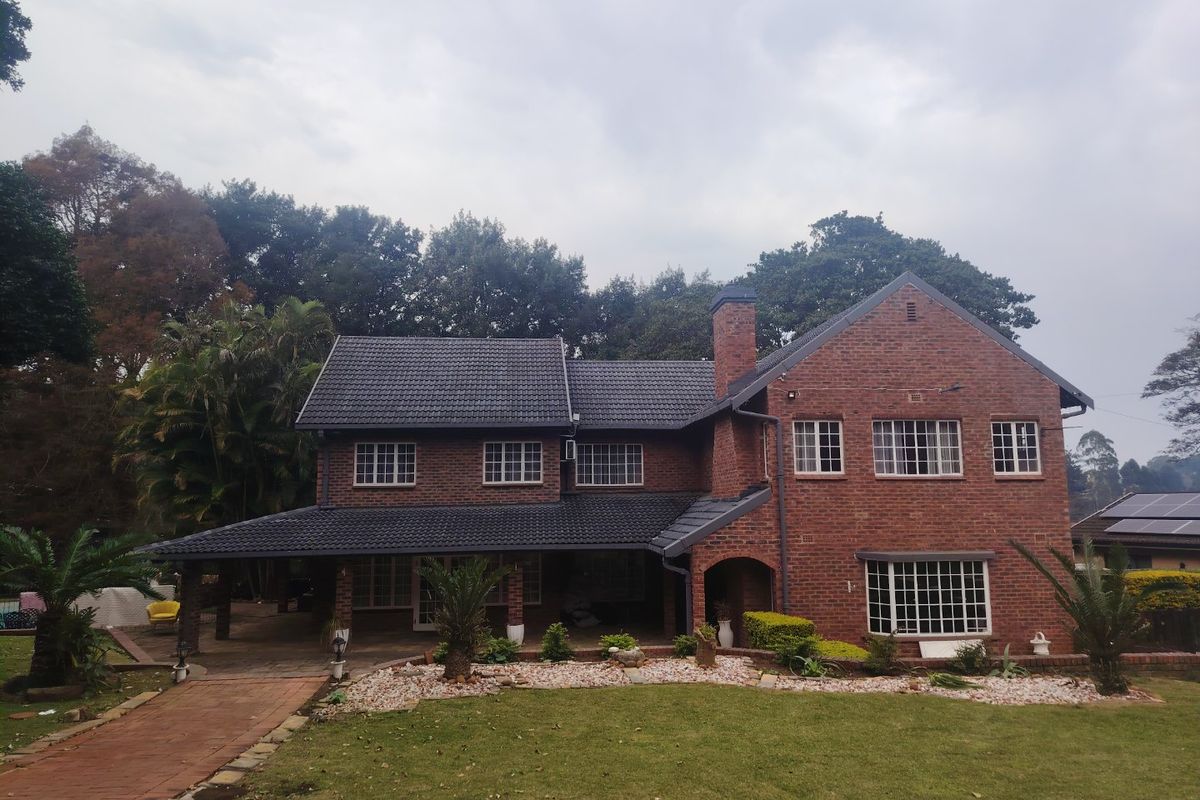 A well-maintained double-story brick house featuring a tiled roof, covered patio area, and established garden with a paved walkway.