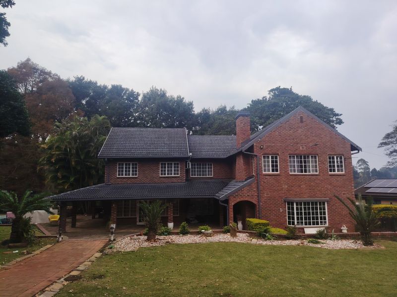 A well-maintained double-story brick house featuring a tiled roof, covered patio area, and established garden with a paved walkway.