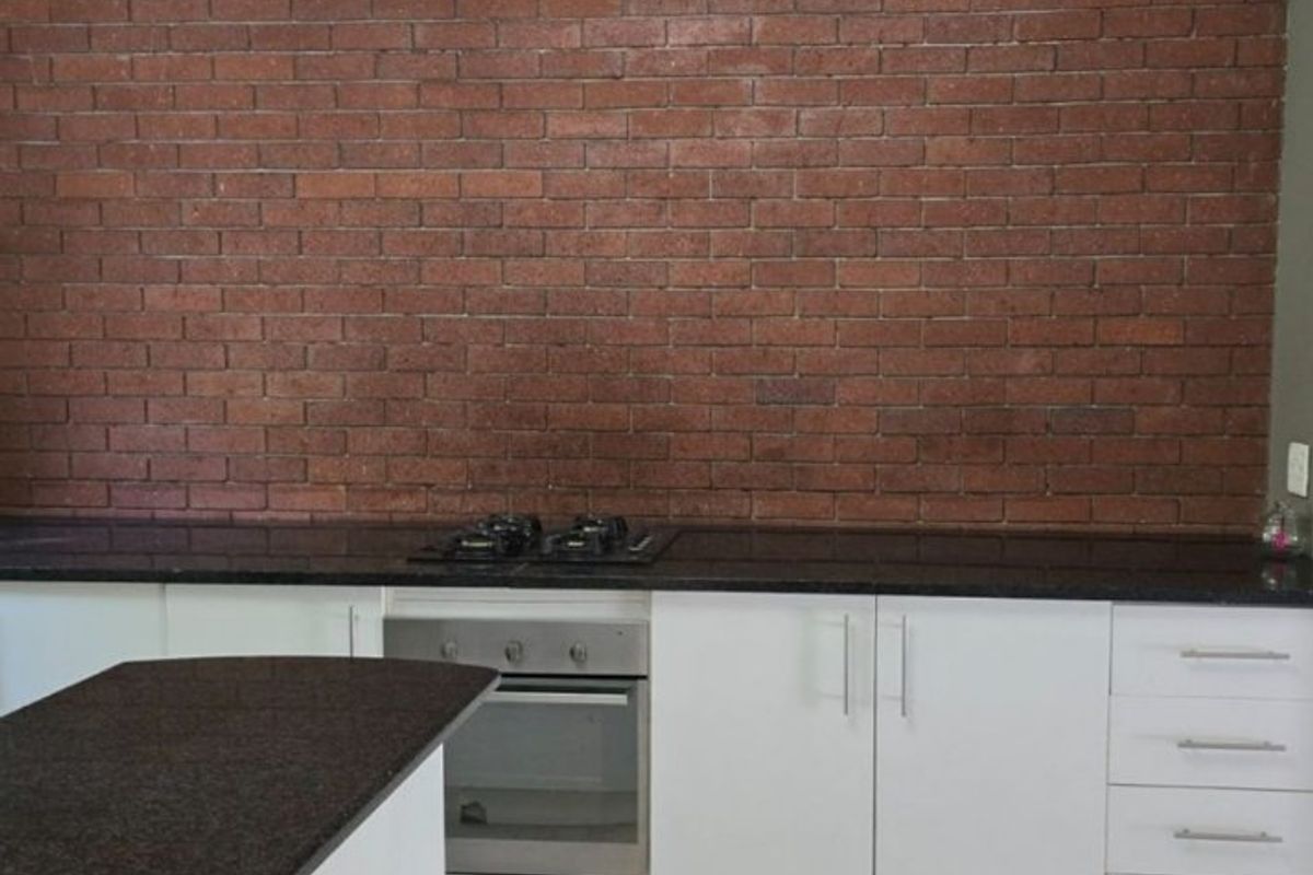 Modern kitchen featuring a striking exposed brick wall, granite countertops, white cabinetry, and a built-in oven with gas hob.
