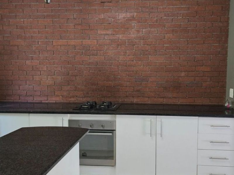 Modern kitchen featuring a striking exposed brick wall, granite countertops, white cabinetry, and a built-in oven with gas hob.