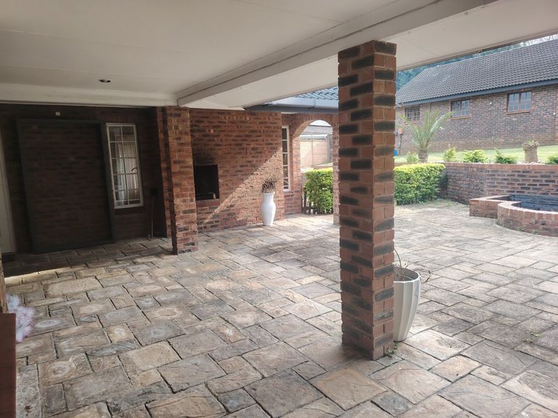 A spacious covered patio featuring brick pillars, a built-in braai, and paved flooring, offering a functional outdoor entertainment area.