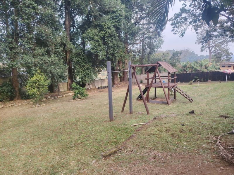 Spacious backyard garden featuring mature trees, a wooden jungle gym, and a pull-up bar, offering a private outdoor recreational space.