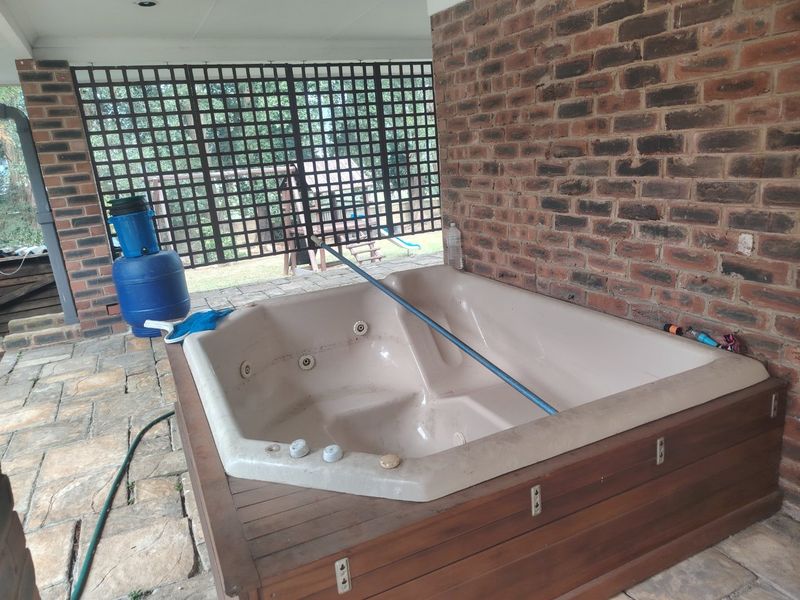 Covered patio area featuring a built-in spa, exposed brick wall, and timber lattice screening, set on stone paving.