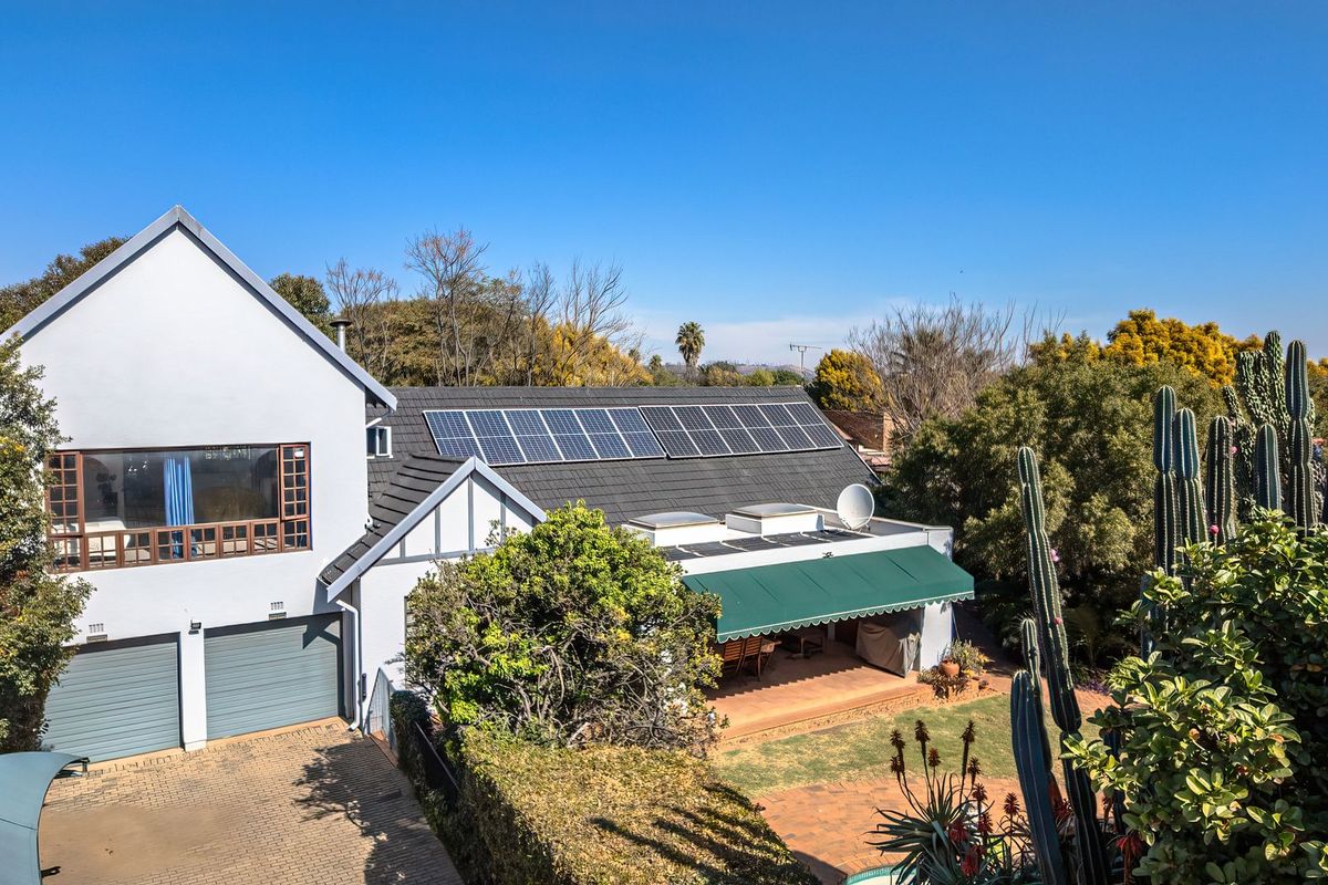 Rear view of a well-maintained house featuring a tiled roof with solar panels, a covered patio with an awning, and a landscaped garden.