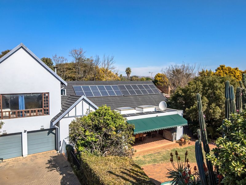 Rear view of a well-maintained house featuring a tiled roof with solar panels, a covered patio with an awning, and a landscaped garden.
