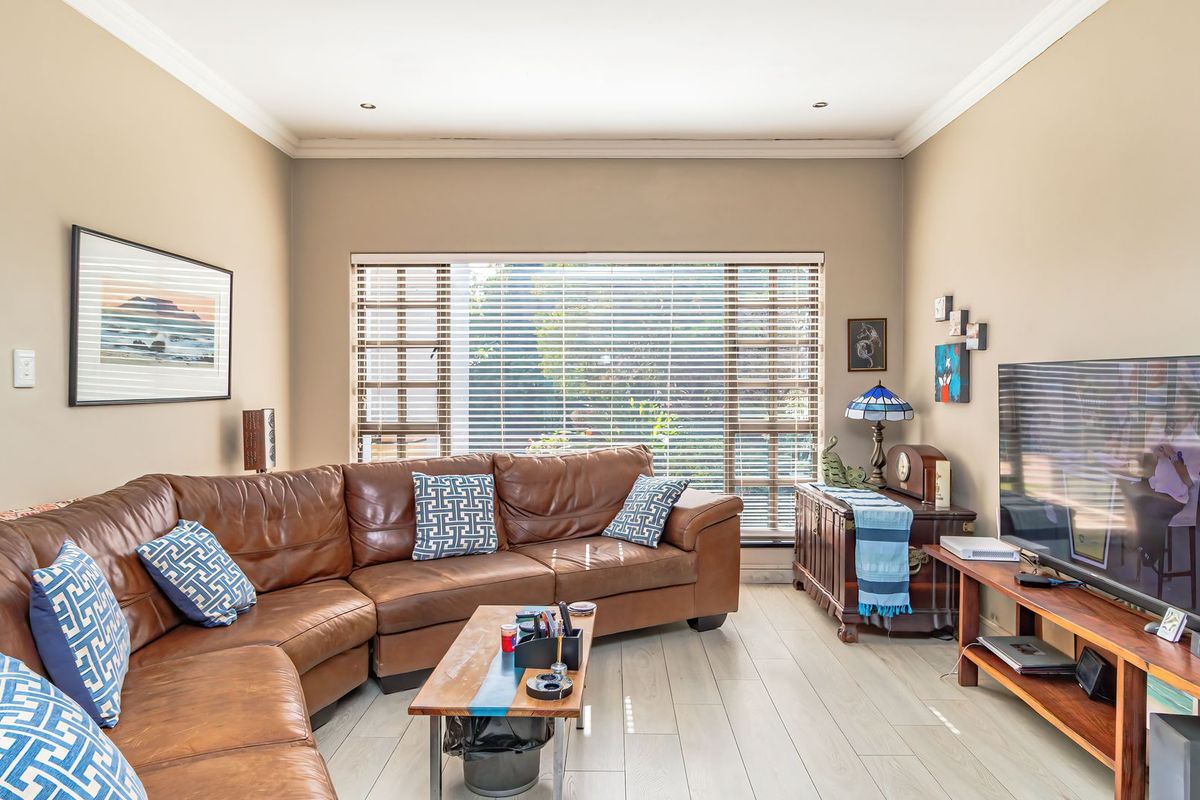 A comfortable living room featuring tiled flooring, recessed downlighting, and large windows fitted with venetian blinds, creating a bright and inviting space.