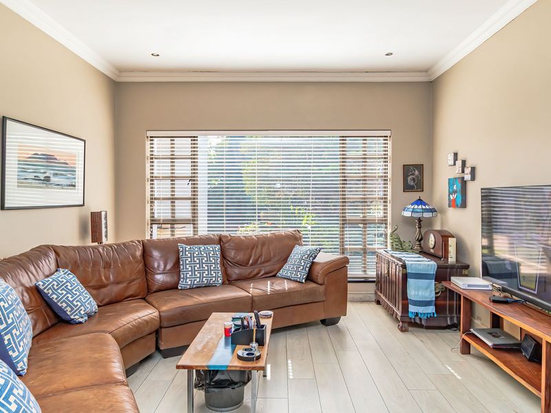 A comfortable living room featuring tiled flooring, recessed downlighting, and large windows fitted with venetian blinds, creating a bright and inviting space.