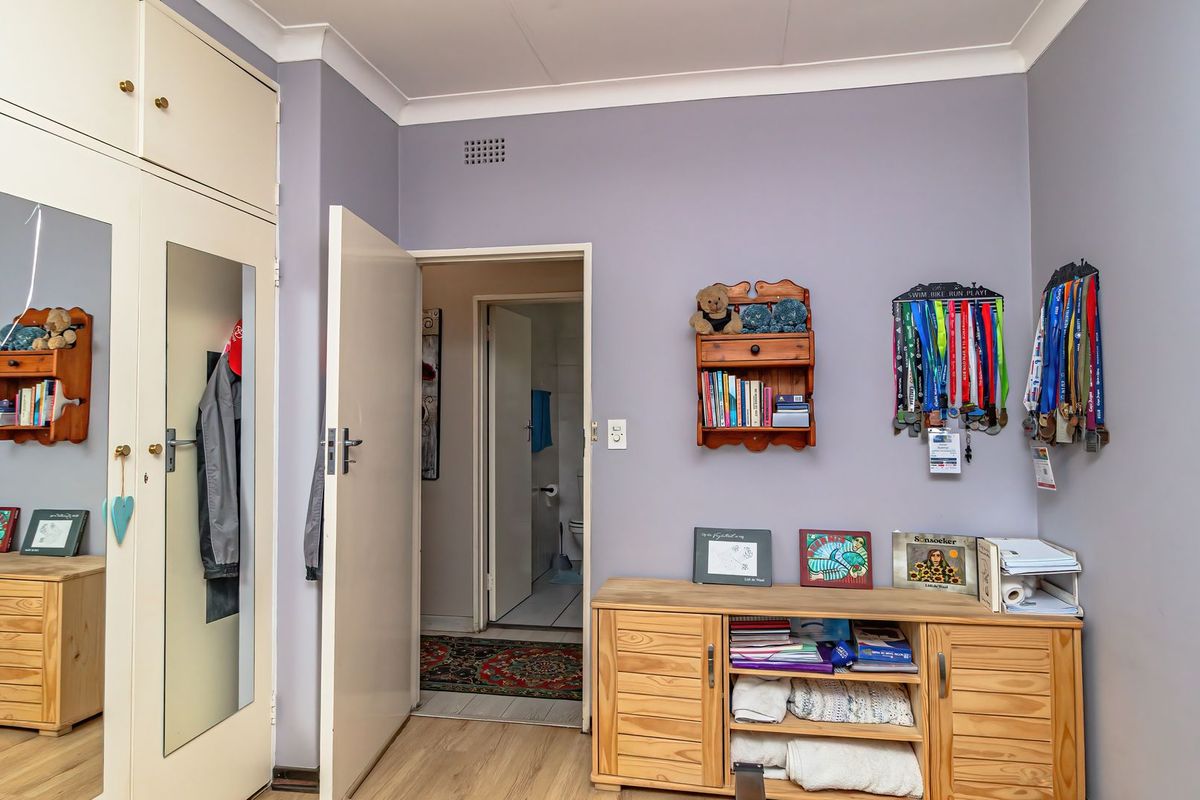A bedroom featuring built-in cupboards with mirrored doors, laminate flooring, and cove cornicing, with an adjacent doorway leading to a bathroom.