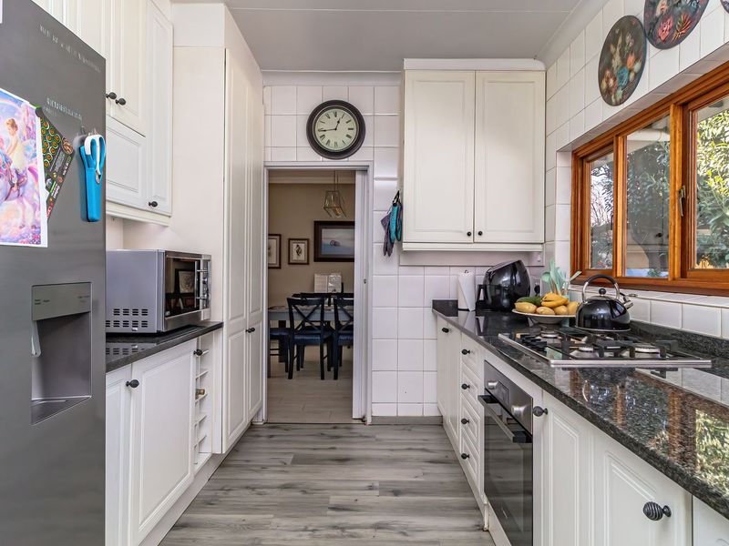 A functional kitchen featuring white cabinetry, granite countertops, a built-in oven, gas hob, and tiled backsplash with views to the garden.