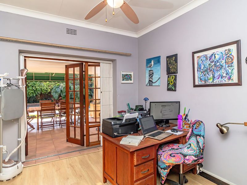 A functional home office space featuring laminate flooring, a ceiling fan, and direct access to an outdoor patio through wooden french doors.