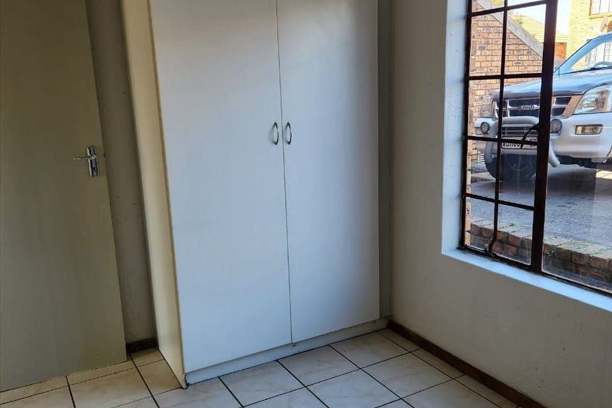 An empty bedroom featuring built-in cupboards, tiled flooring, and a steel-framed window looking out onto the driveway.
