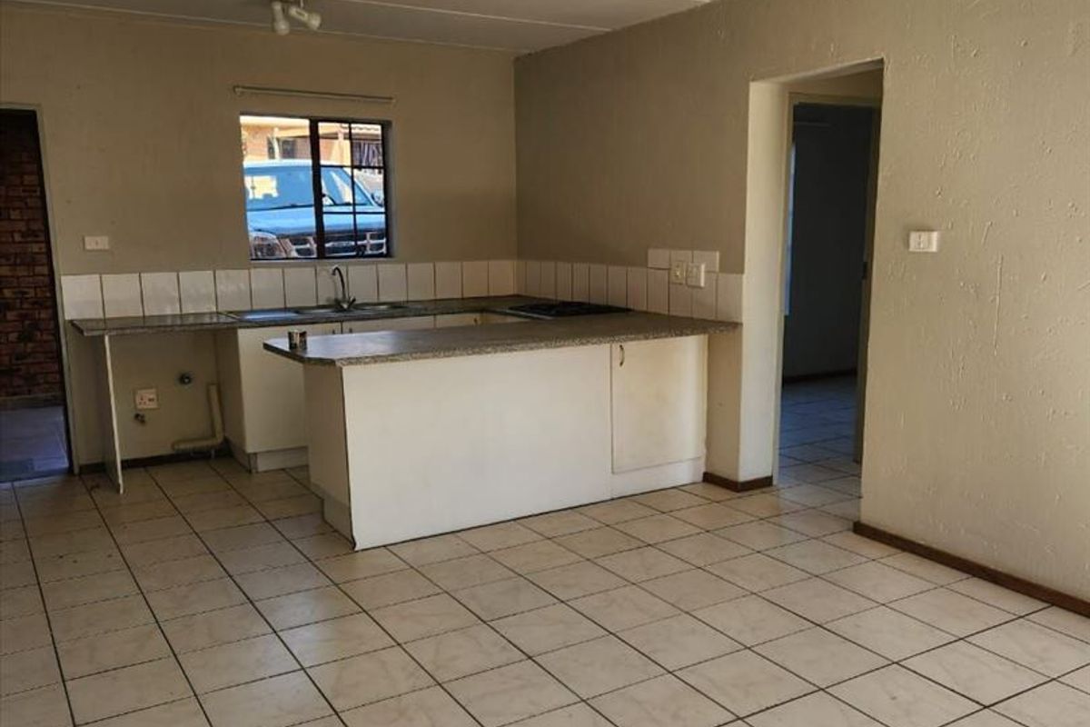 Open-plan kitchen and living area featuring tiled flooring, built-in cabinetry with a breakfast counter, and a functional hob, presenting a blank canvas for renovation.