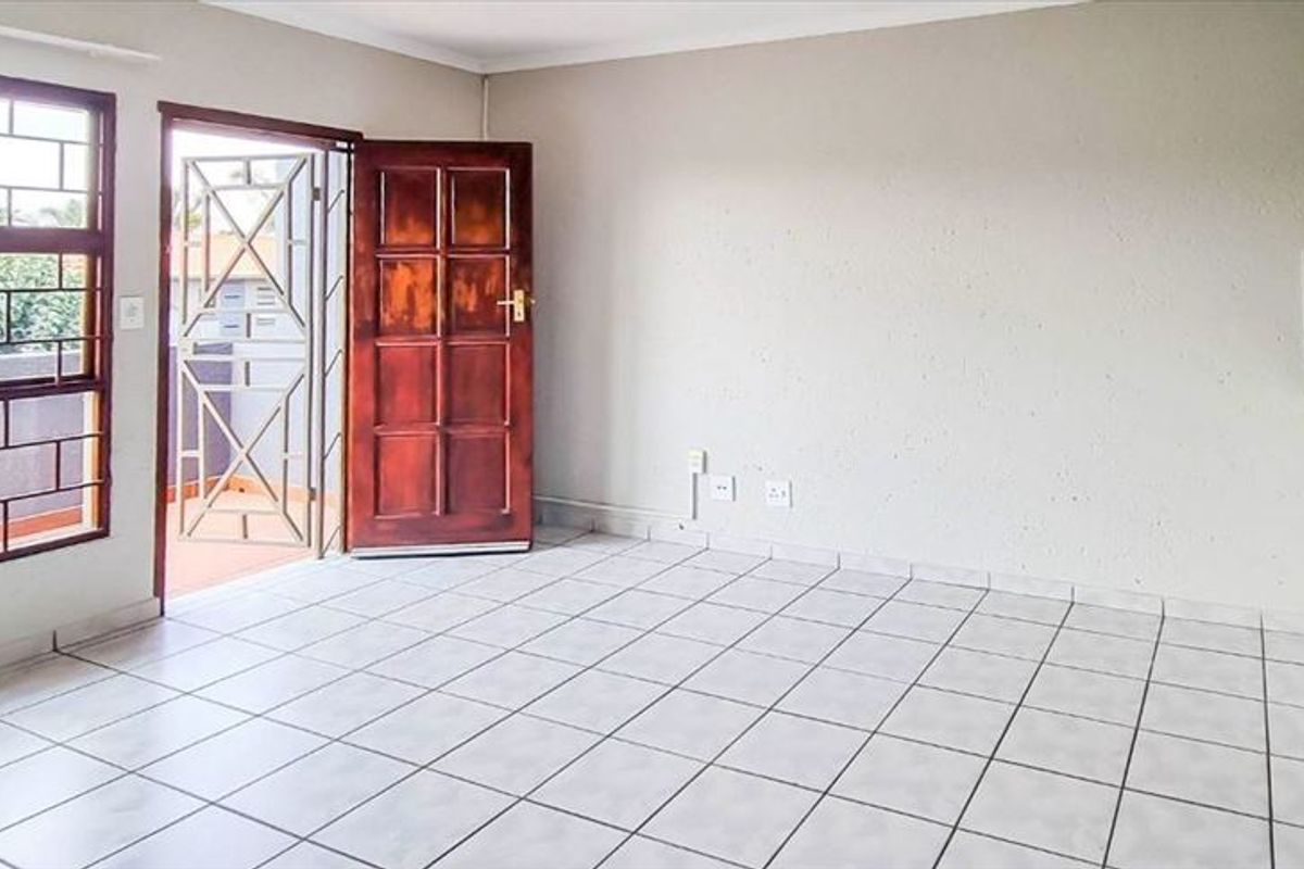 An open-plan living area featuring tiled flooring, a security gate, and a kitchen counter with tiled splashback, offering a functional and bright space.
