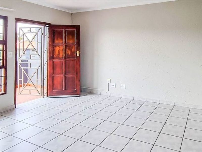 An open-plan living area featuring tiled flooring, a security gate, and a kitchen counter with tiled splashback, offering a functional and bright space.