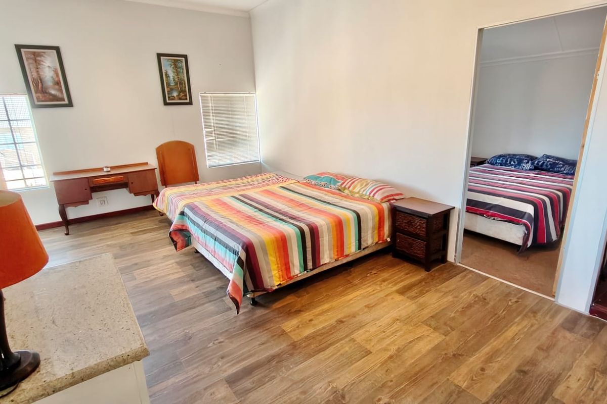 A bedroom featuring laminate flooring and natural light through venetian blinds, with an adjoining room visible through the doorway.