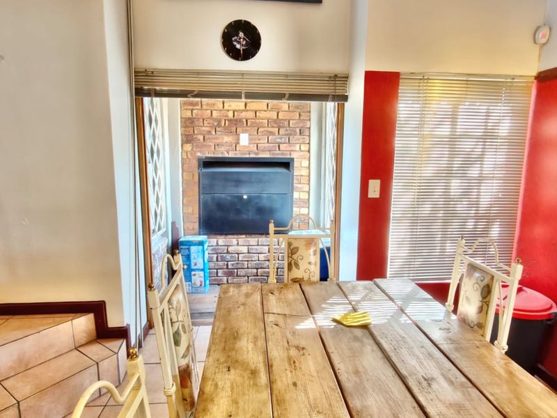 Dining area featuring a built-in brick fireplace, tiled flooring, and natural light through venetian blinds.