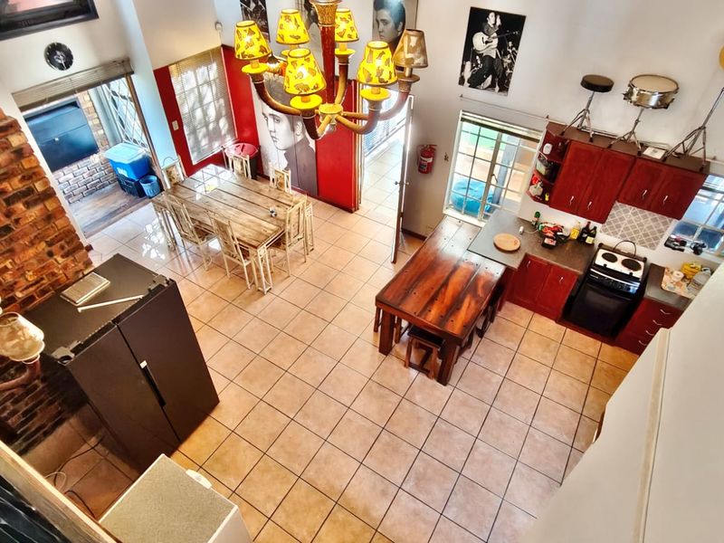 Spacious open-plan living and kitchen area featuring high ceilings, an exposed brick fireplace, and tiled flooring throughout.
