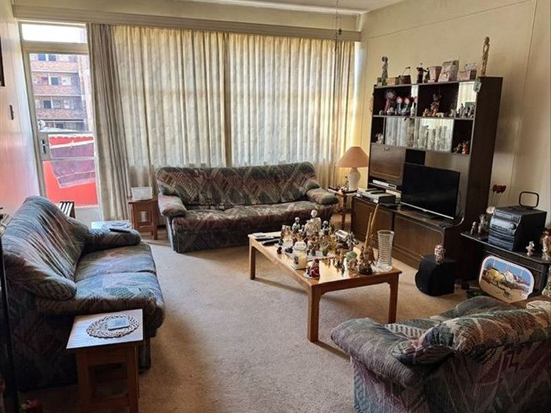 A spacious living room featuring large windows with curtain tracks, a ceiling fan, and access to an outdoor balcony area.