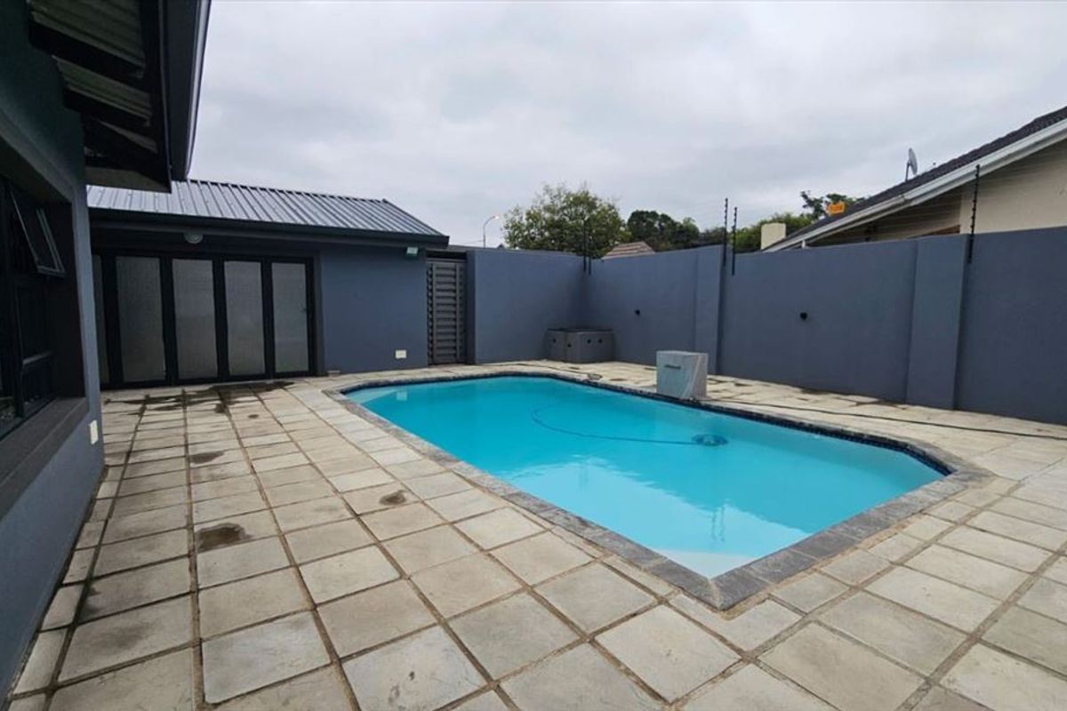A private outdoor pool area featuring a paved patio, enclosed by high boundary walls with electric fencing and direct access to the home.