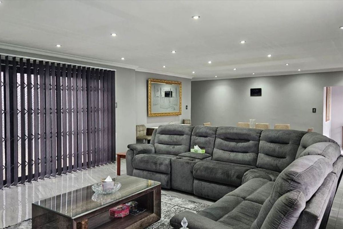 Spacious living room featuring polished tiled flooring, recessed downlighting, and a secure sliding gate leading to the exterior.