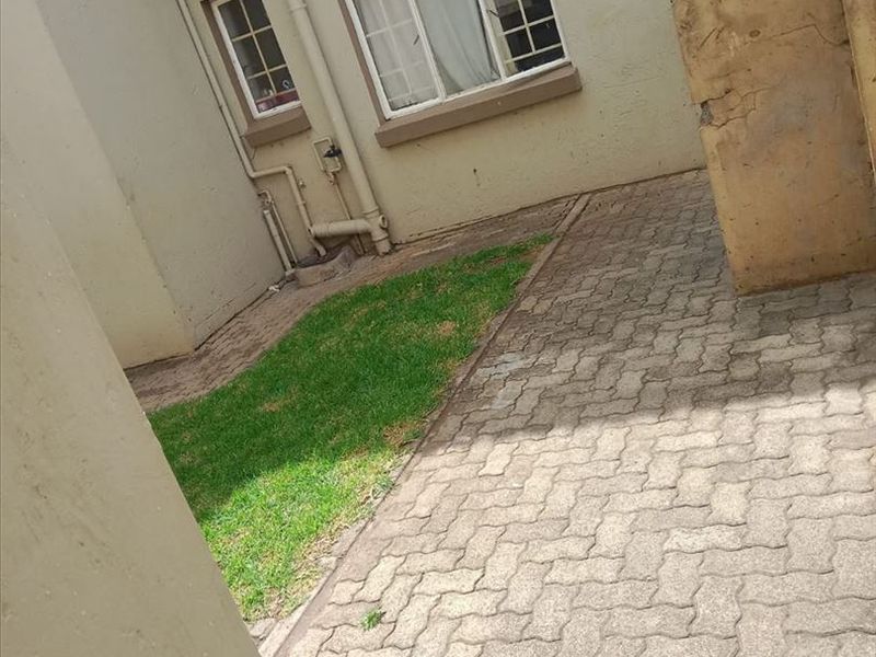 A small rear courtyard featuring paved flooring, a compact lawn area, and exterior building access with visible masonry and paint wear.