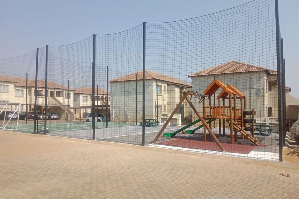 Communal sports facility featuring a fenced court and playground area situated within a townhouse complex.