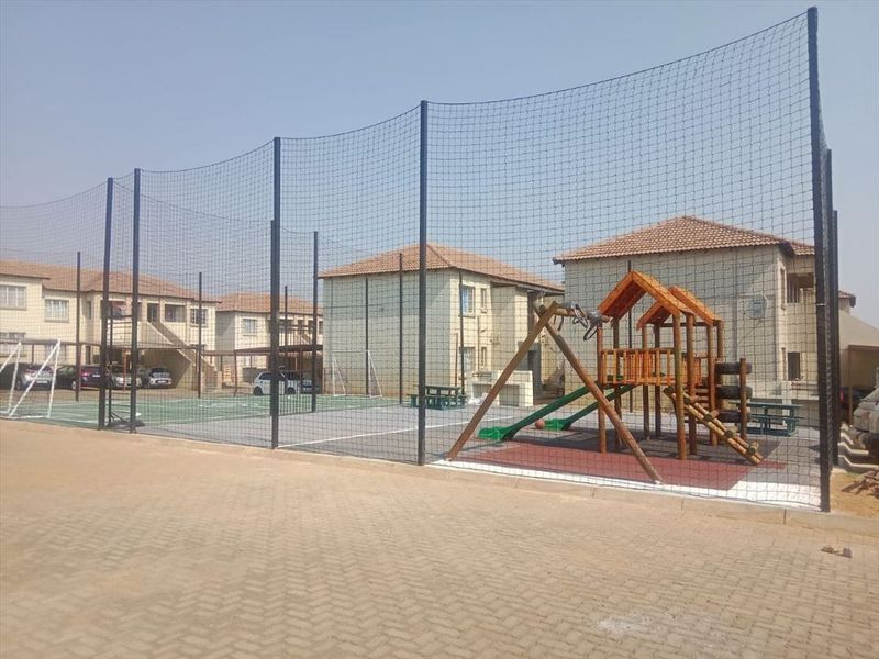 Communal sports facility featuring a fenced court and playground area situated within a townhouse complex.