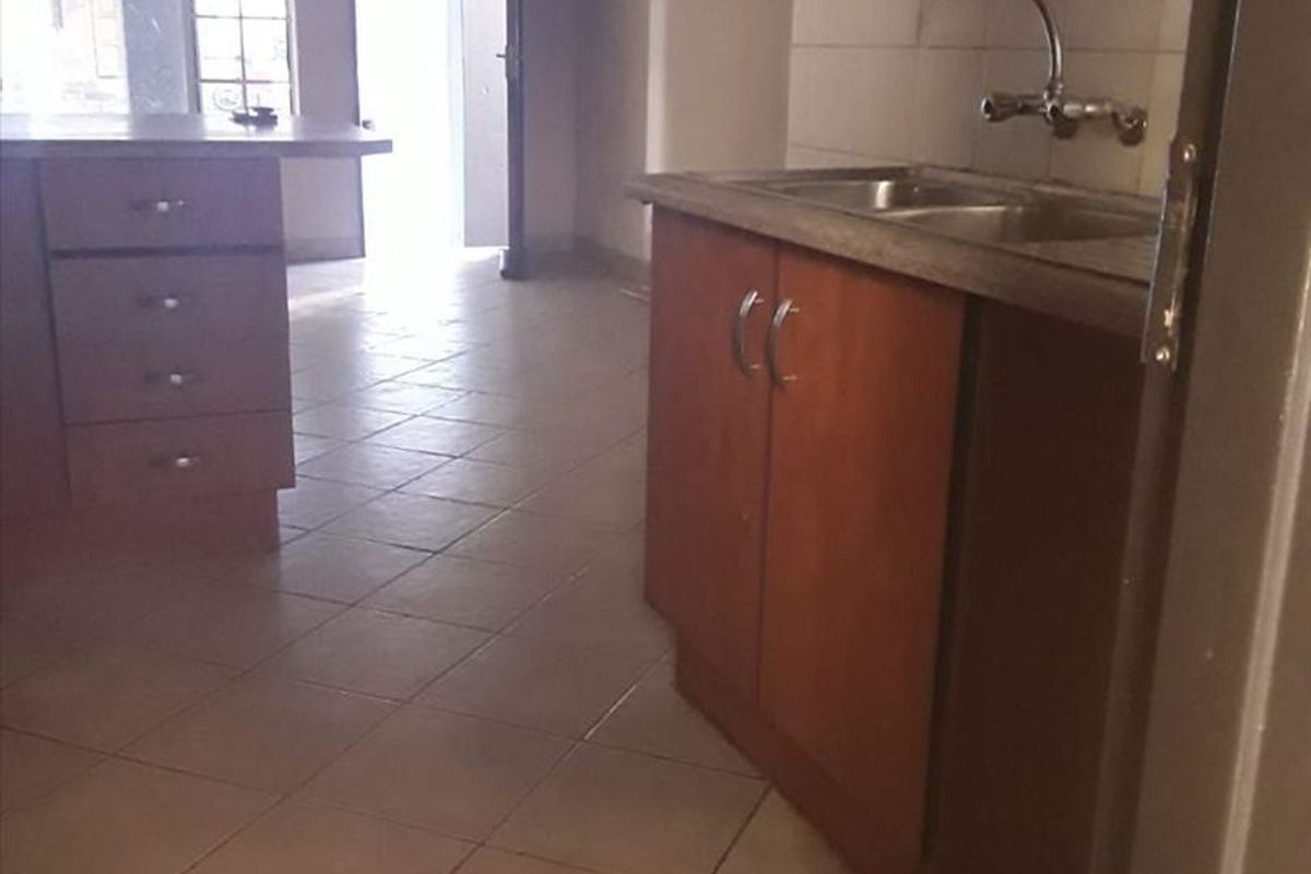 An empty kitchen area featuring wooden cabinetry, a double sink, and tiled flooring, offering a blank canvas for potential renovation and modernization.