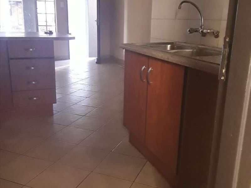 An empty kitchen area featuring wooden cabinetry, a double sink, and tiled flooring, offering a blank canvas for potential renovation and modernization.
