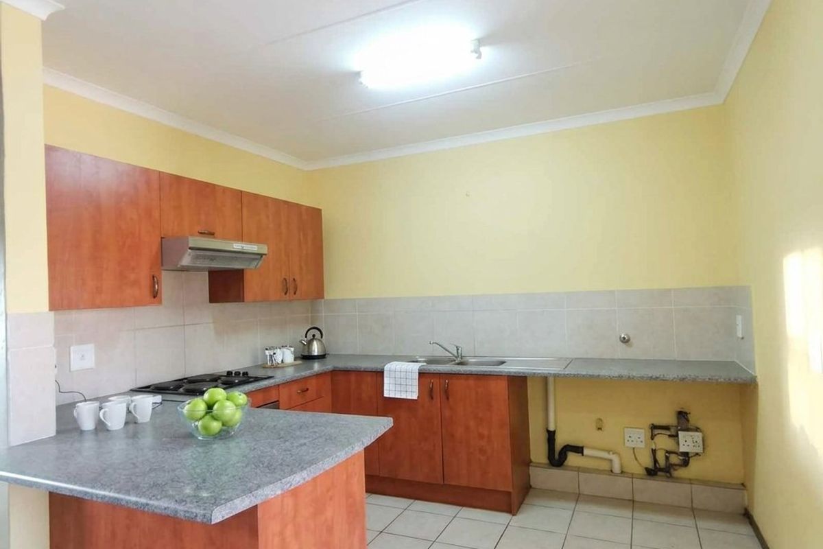 A functional kitchen featuring laminate cabinetry, stone-look countertops, a built-in gas hob with extractor fan, and tiled flooring.